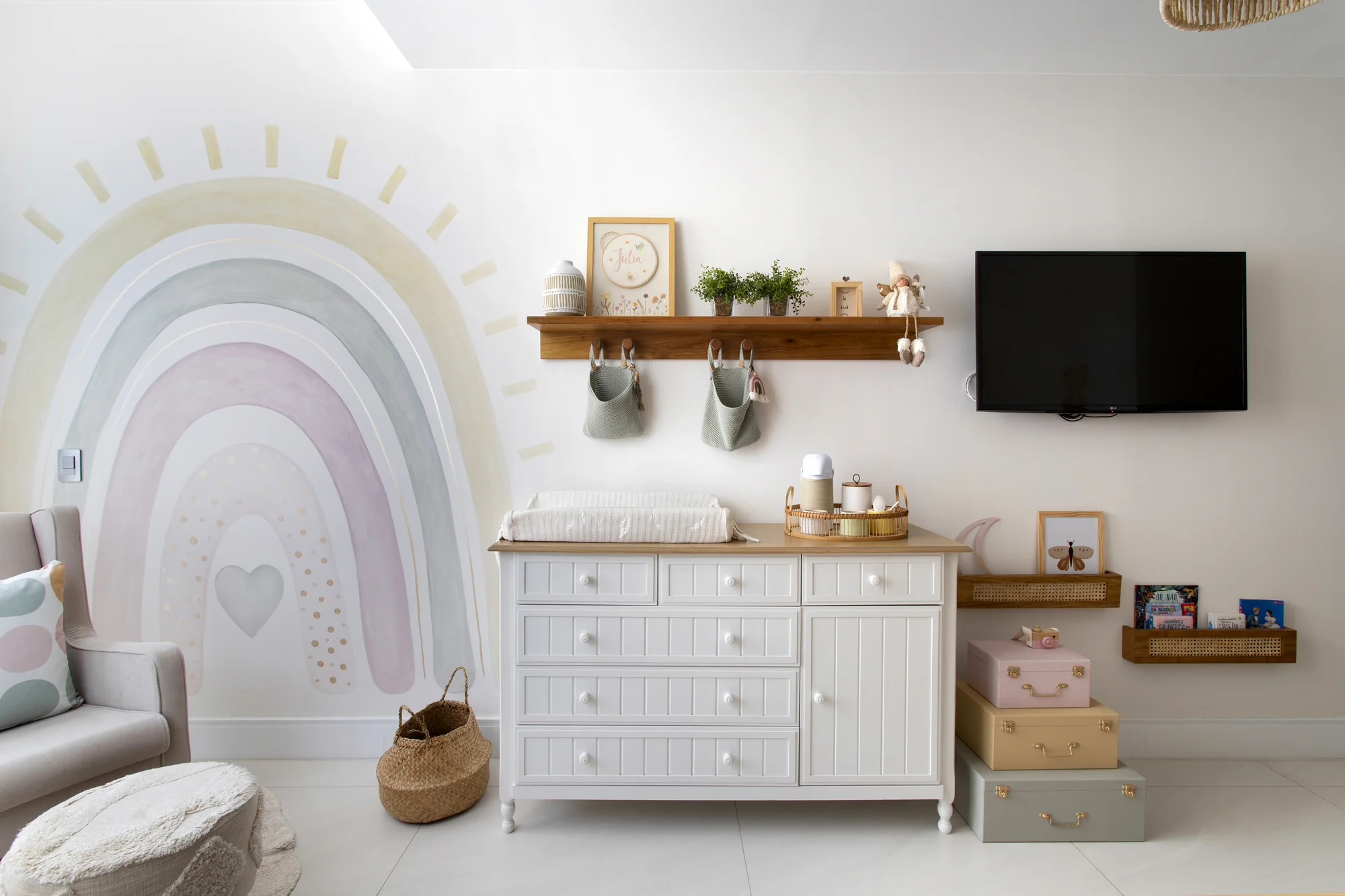 Quarto infantil com arco-íris pintado na parede, cômoda branca e prateleiras de madeira