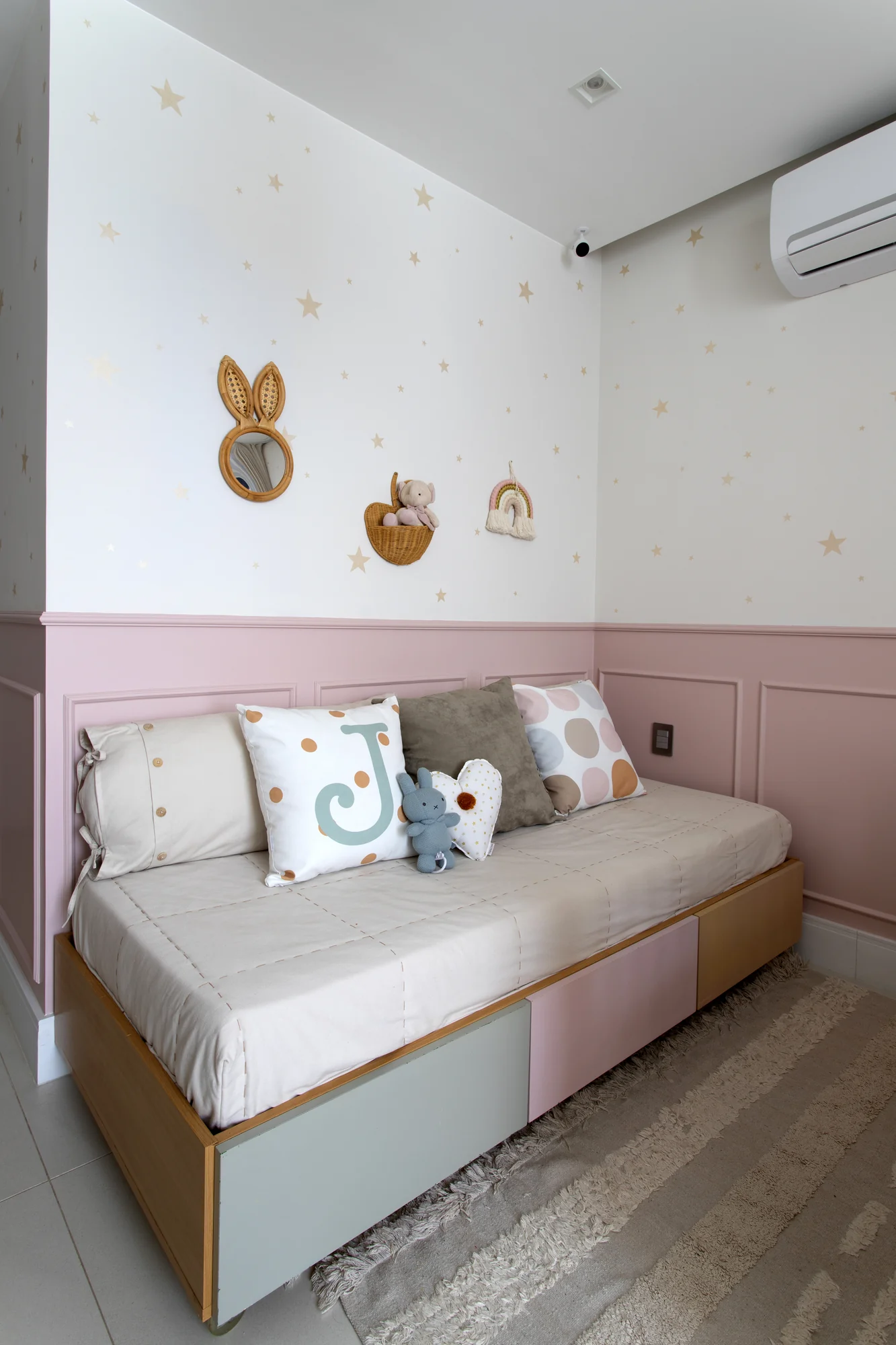 Cama infantil encostada na meia-parede rosa, com apliques de coelho e estrelas