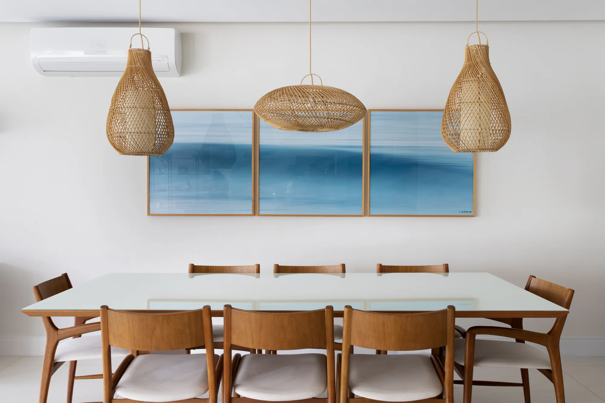 Mesa de jantar branca com cadeiras de madeira e três pendentes de fibra
