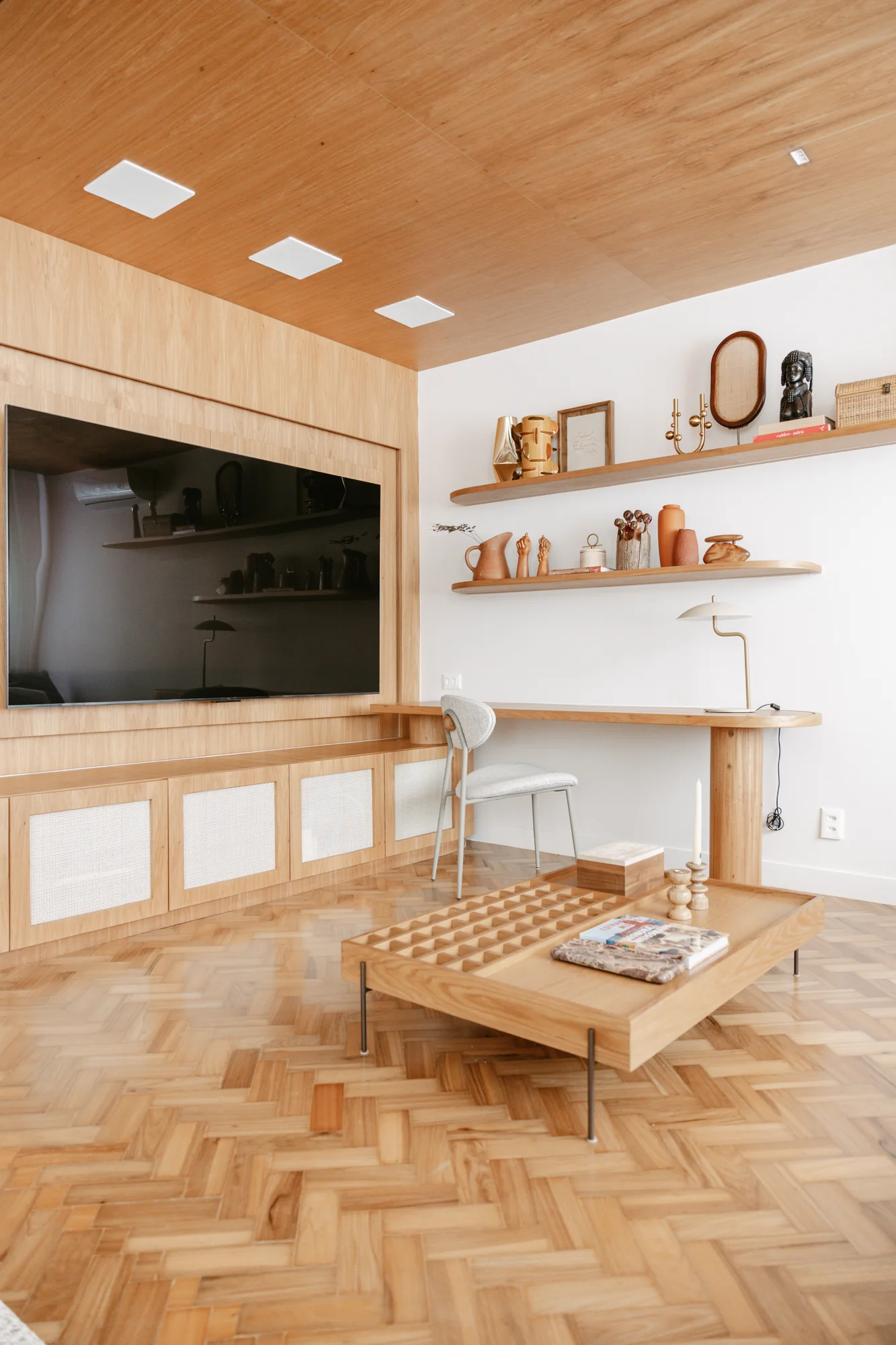 Sala de estar com piso em espinha de peixe, painel de madeira e televisão