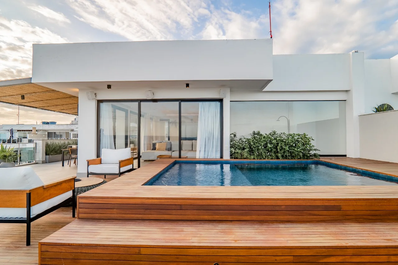 Piscina com deck de madeira no terraço, com poltronas à sombra da cobertura