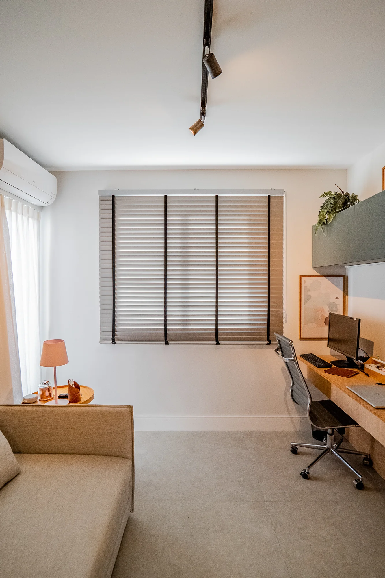 Home office com escrivaninha junto à janela de venezianas e sofá claro