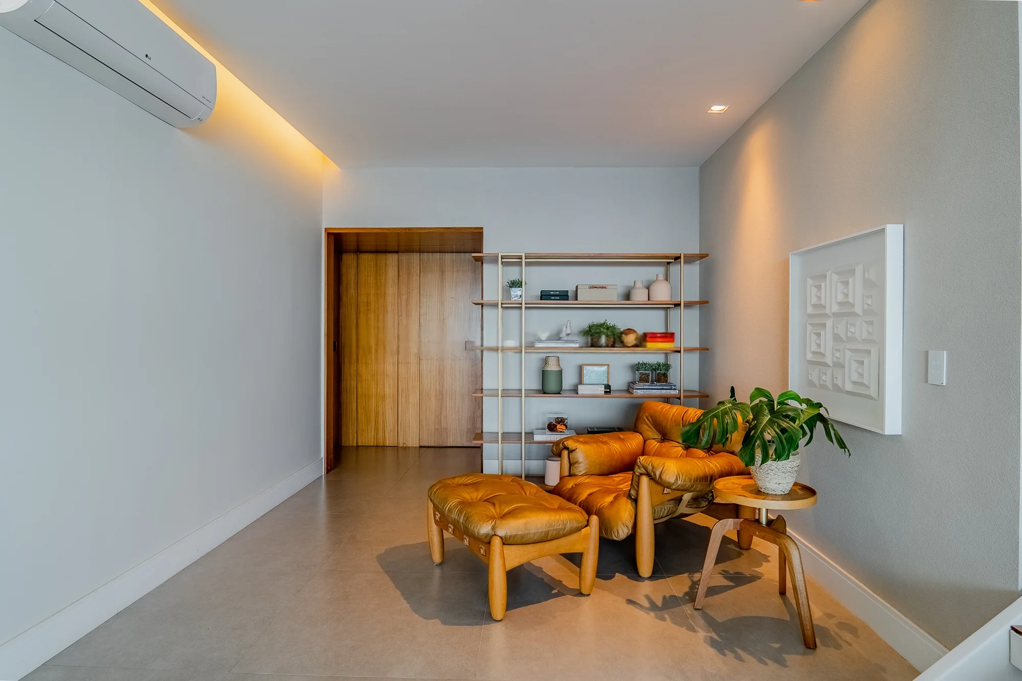 Sala de estar com estante vazada, poltrona de couro caramelo e porta de madeira