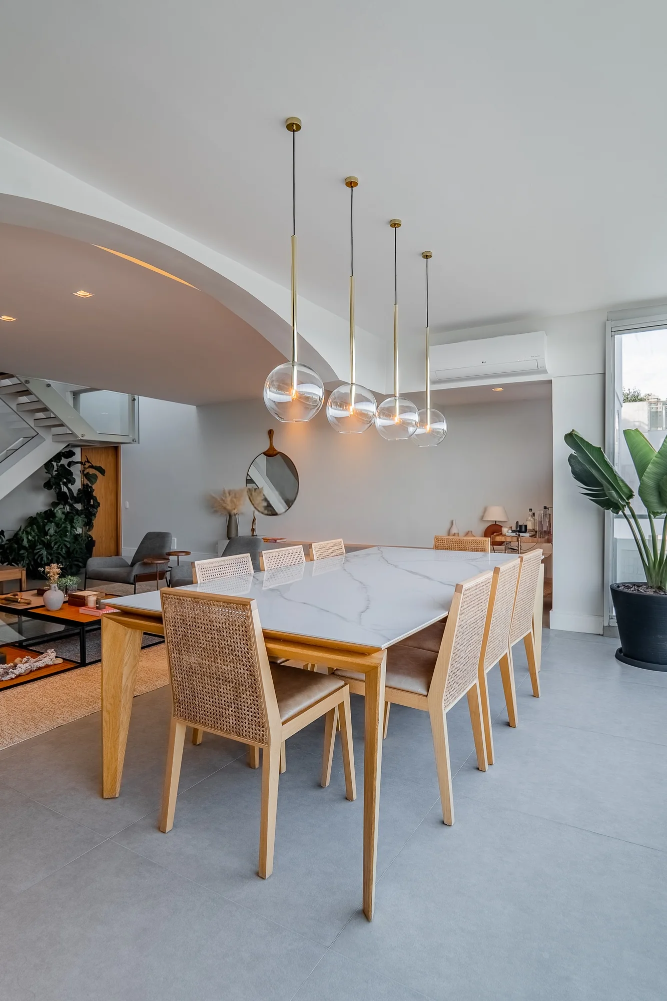 Sala de jantar com mesa de mármore, cadeiras de palhinha e pendentes de vidro