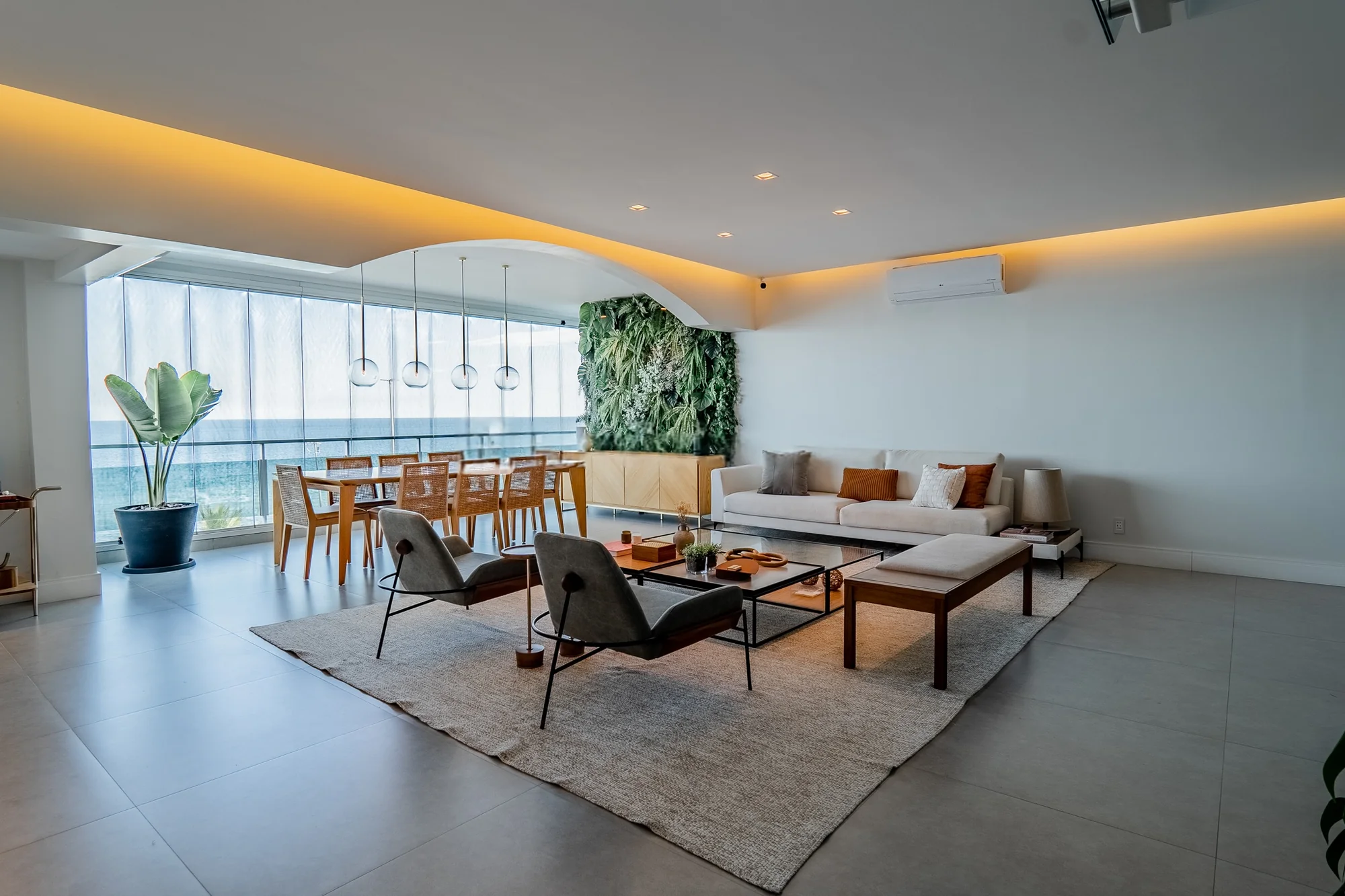 Living e jantar integrados, com jardim vertical, chaise longue e sanca iluminada