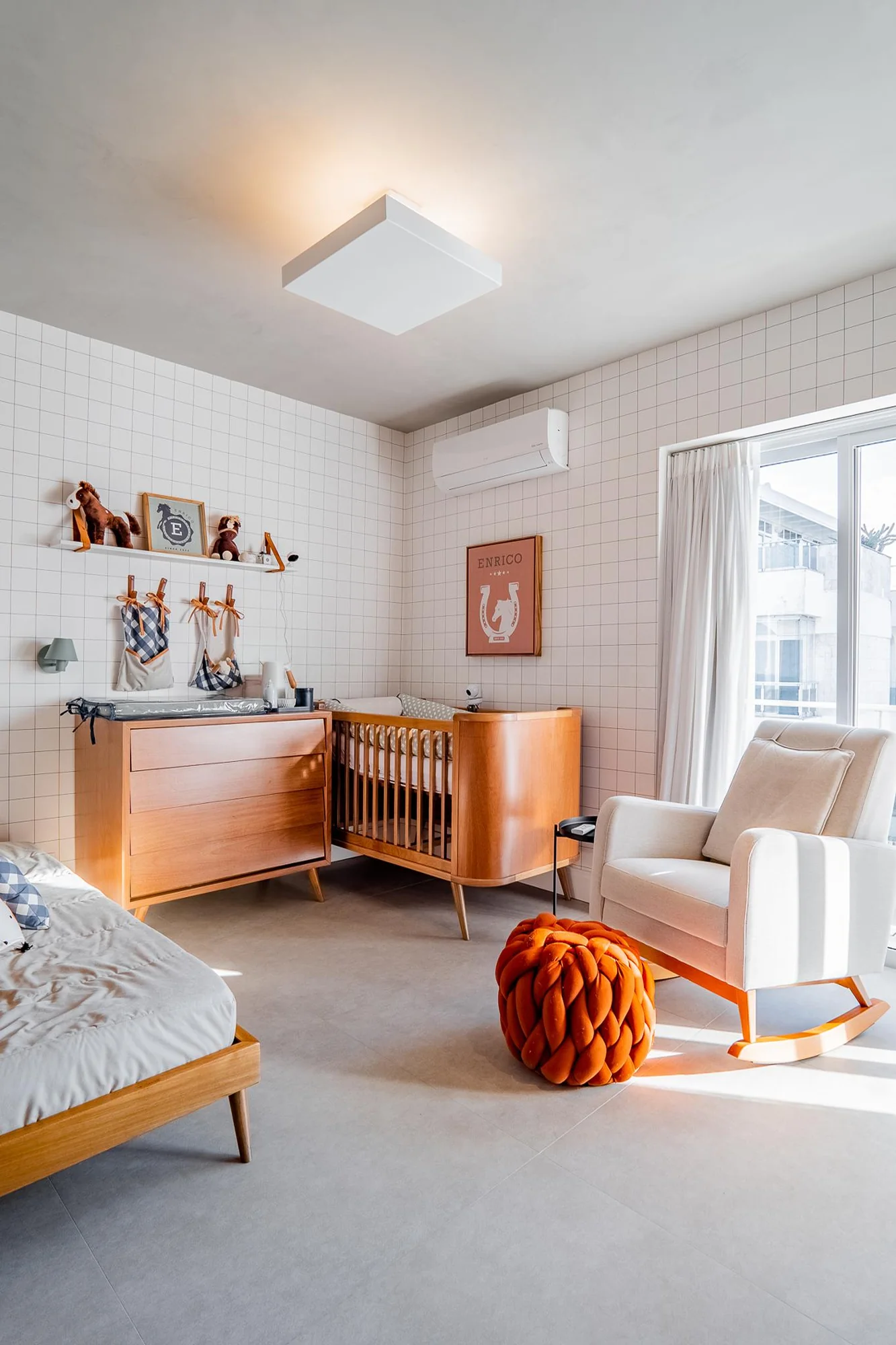 Quarto infantil com berço de madeira, cadeira de balanço e parede de azulejos brancos