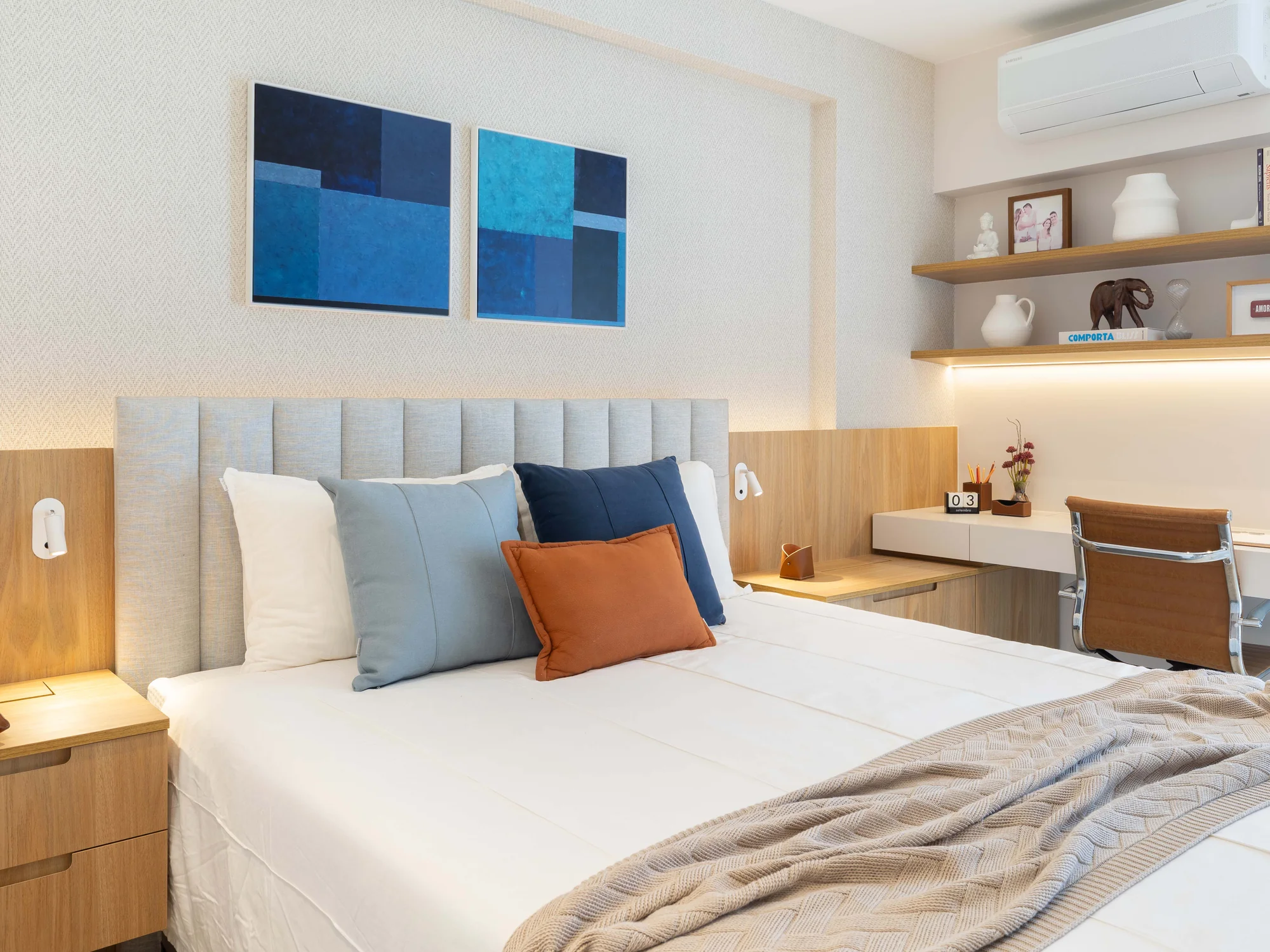 Cama de casal com cabeceira estofada canelada, quadros azuis e criados-mudos de madeira