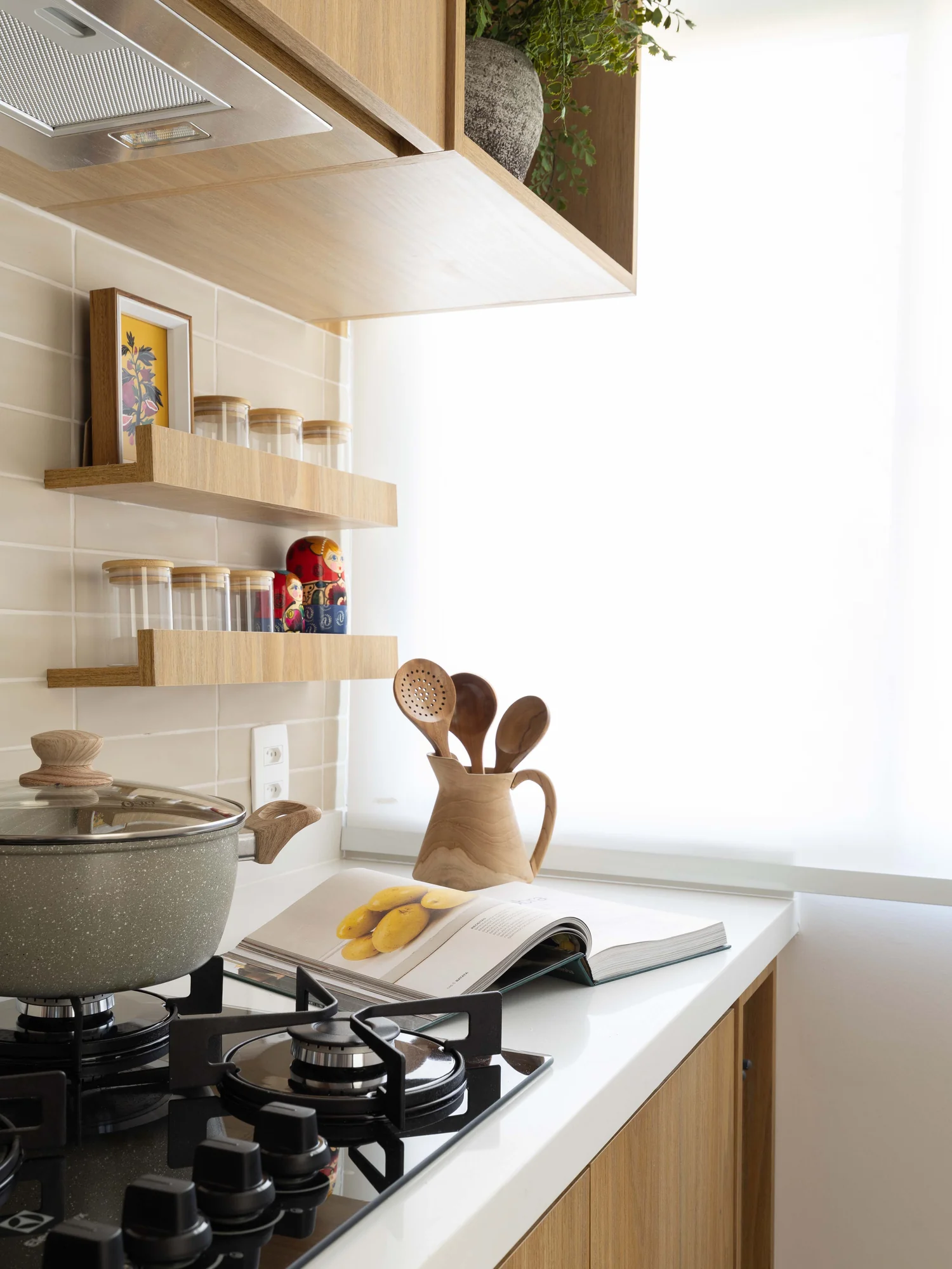 Cooktop com panela sobre a bancada branca e prateleiras de madeira com temperos