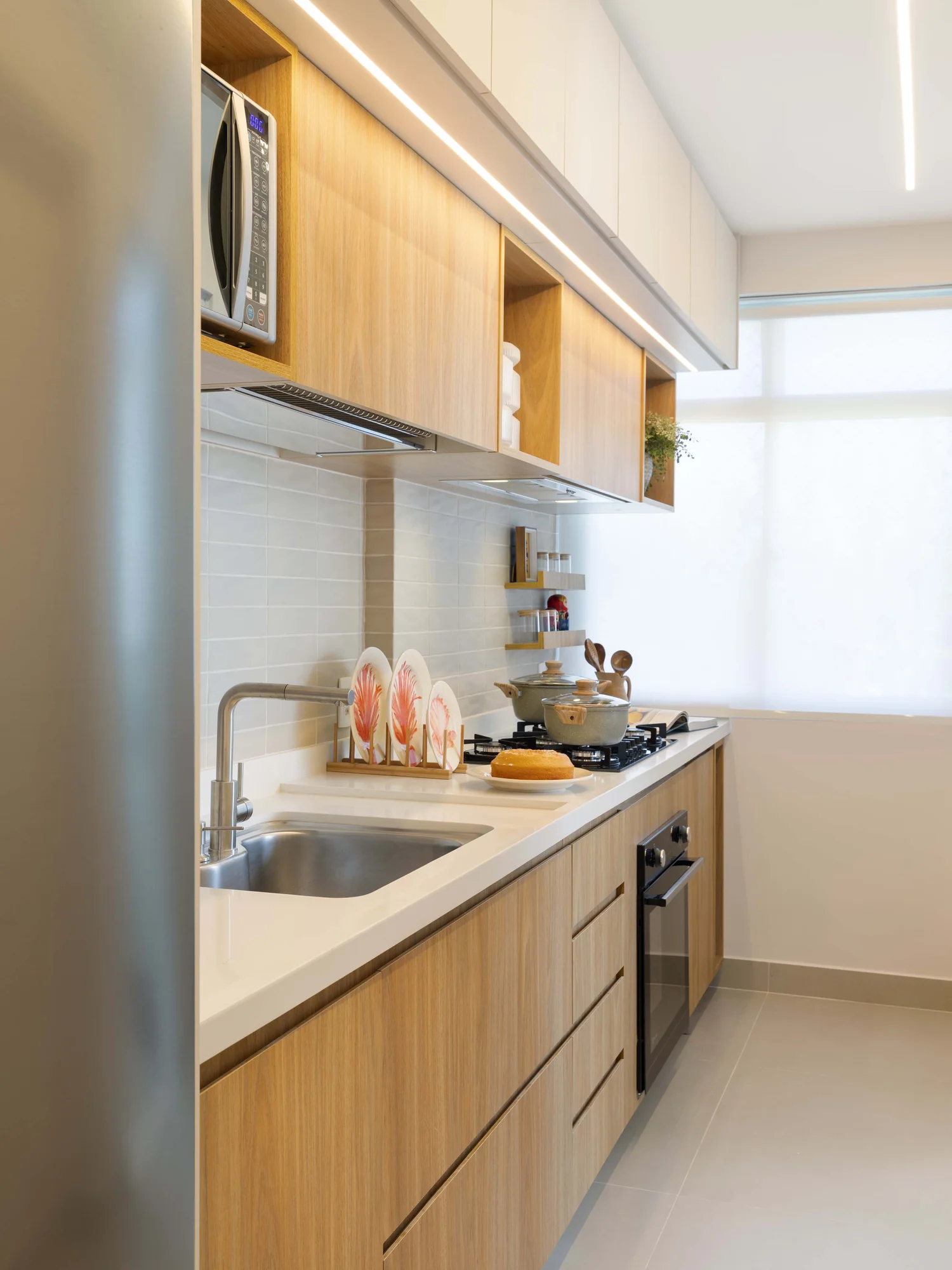Cozinha estreita com geladeira de inox, armários suspensos e bancada de trabalho