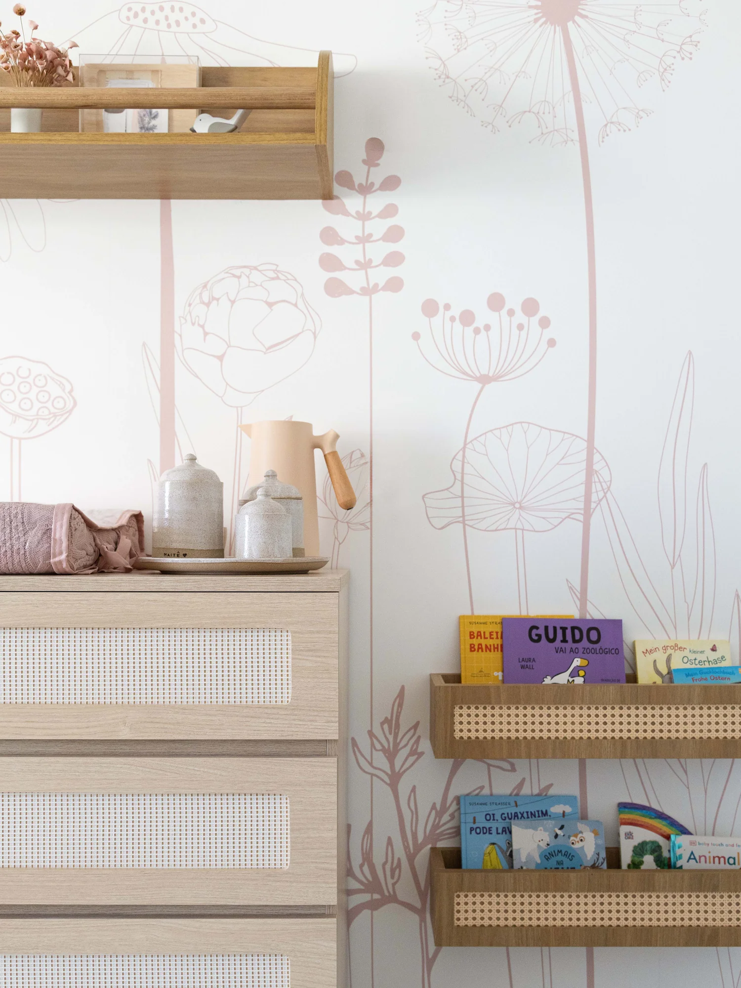 Cômoda de palhinha e prateleiras com livros, sobre papel de parede de flores