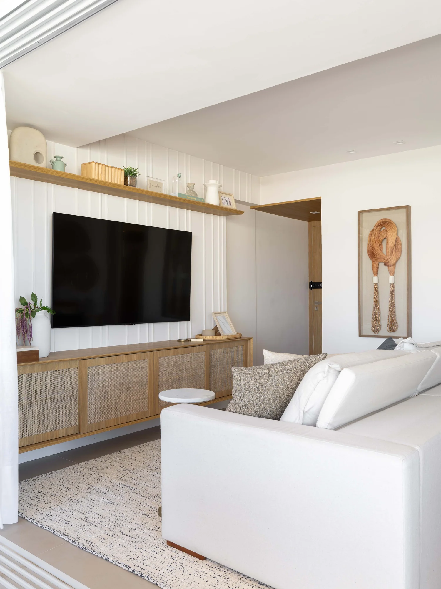 Sala de estar com painel de televisão, sofá branco e prateleira de madeira