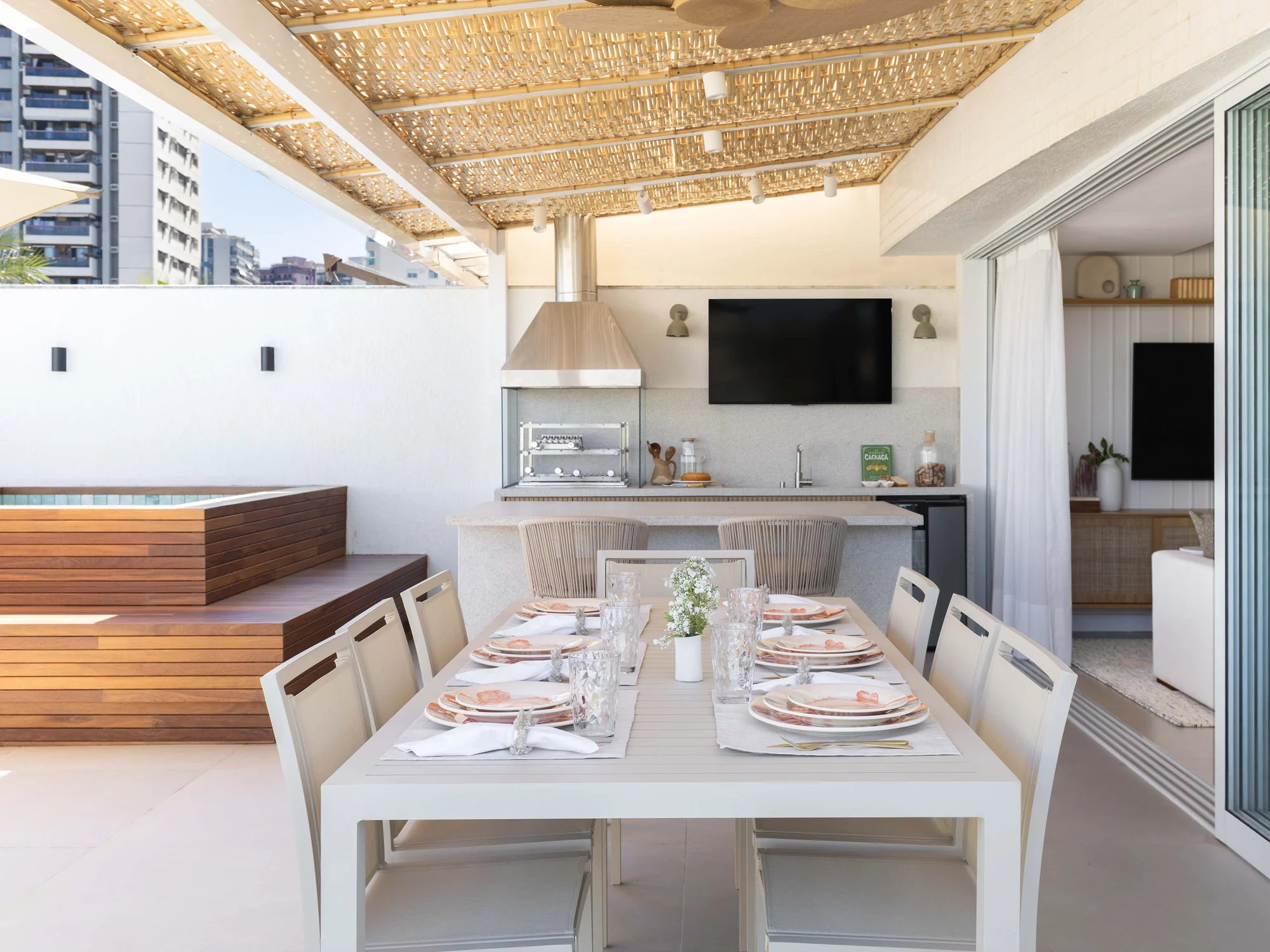 Área gourmet coberta por forro de palha, com mesa posta e vista para a cidade