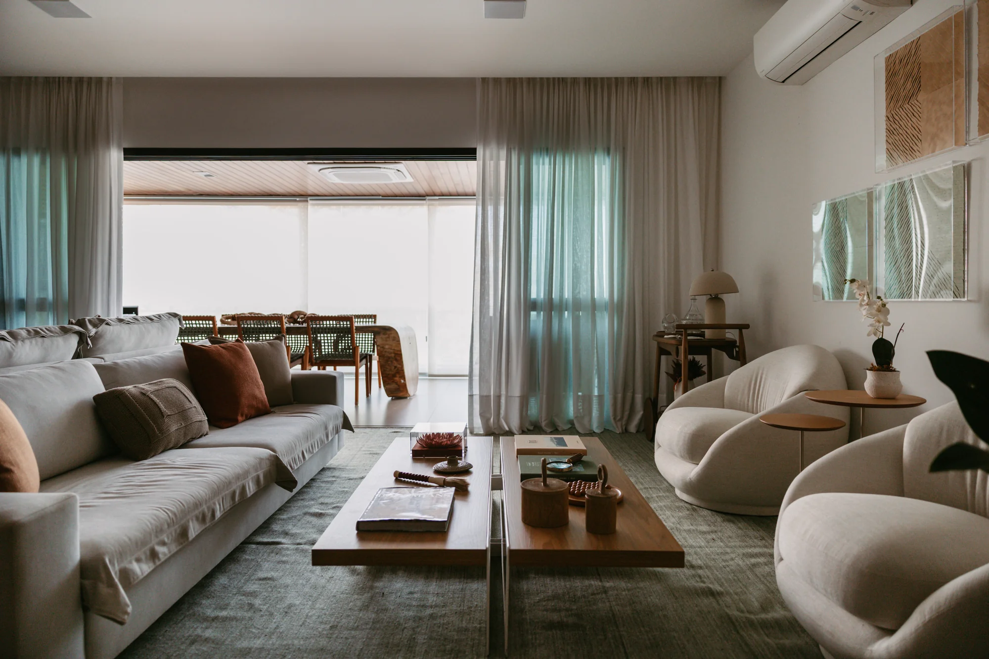 Living em enfiada, com sofá comprido, poltronas e cortina clara