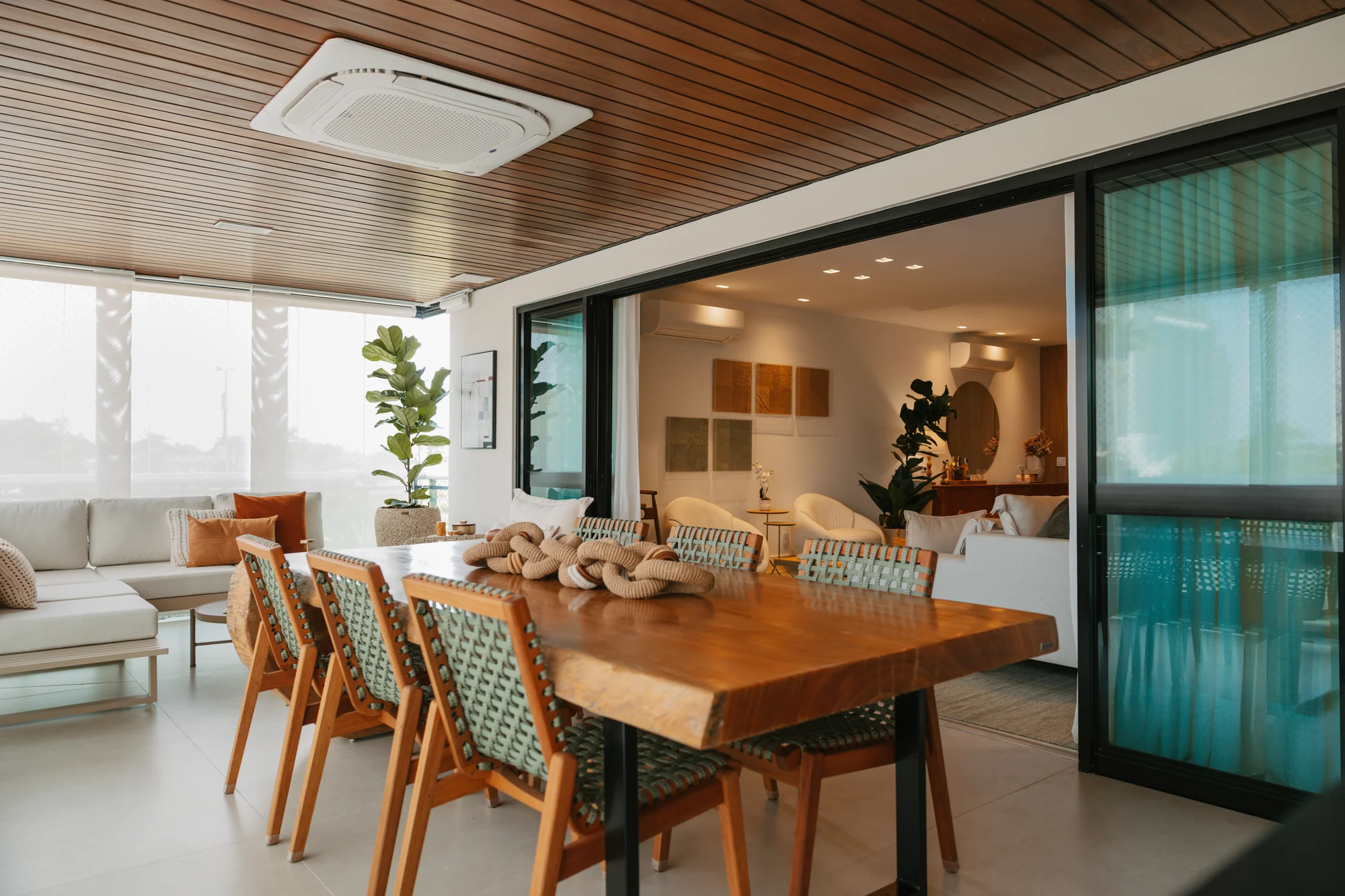 Sala de jantar com forro de madeira, cadeiras verdes e esquadrias escuras