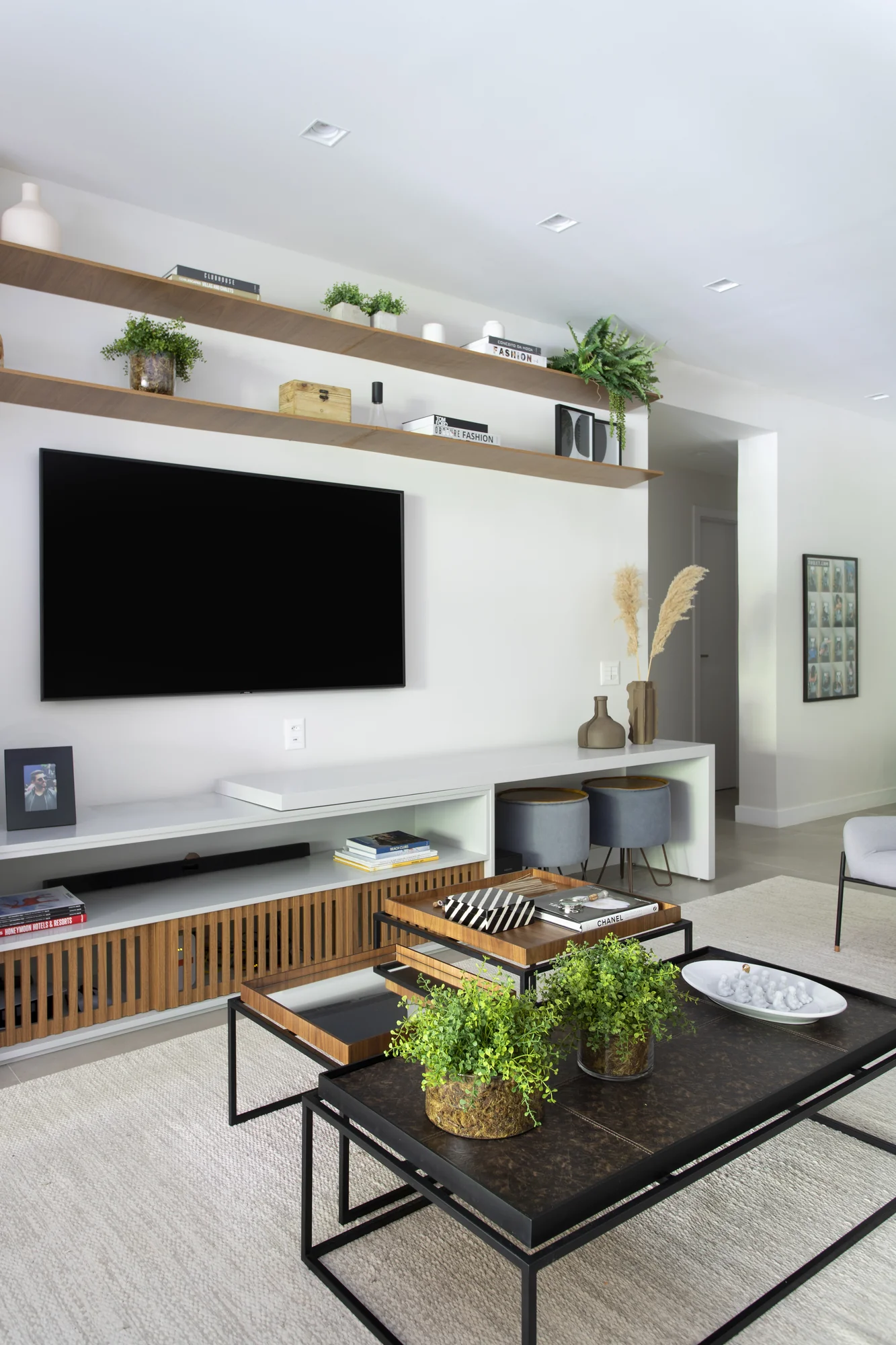 Painel branco com televisão, prateleiras de madeira e mesa de centro escura