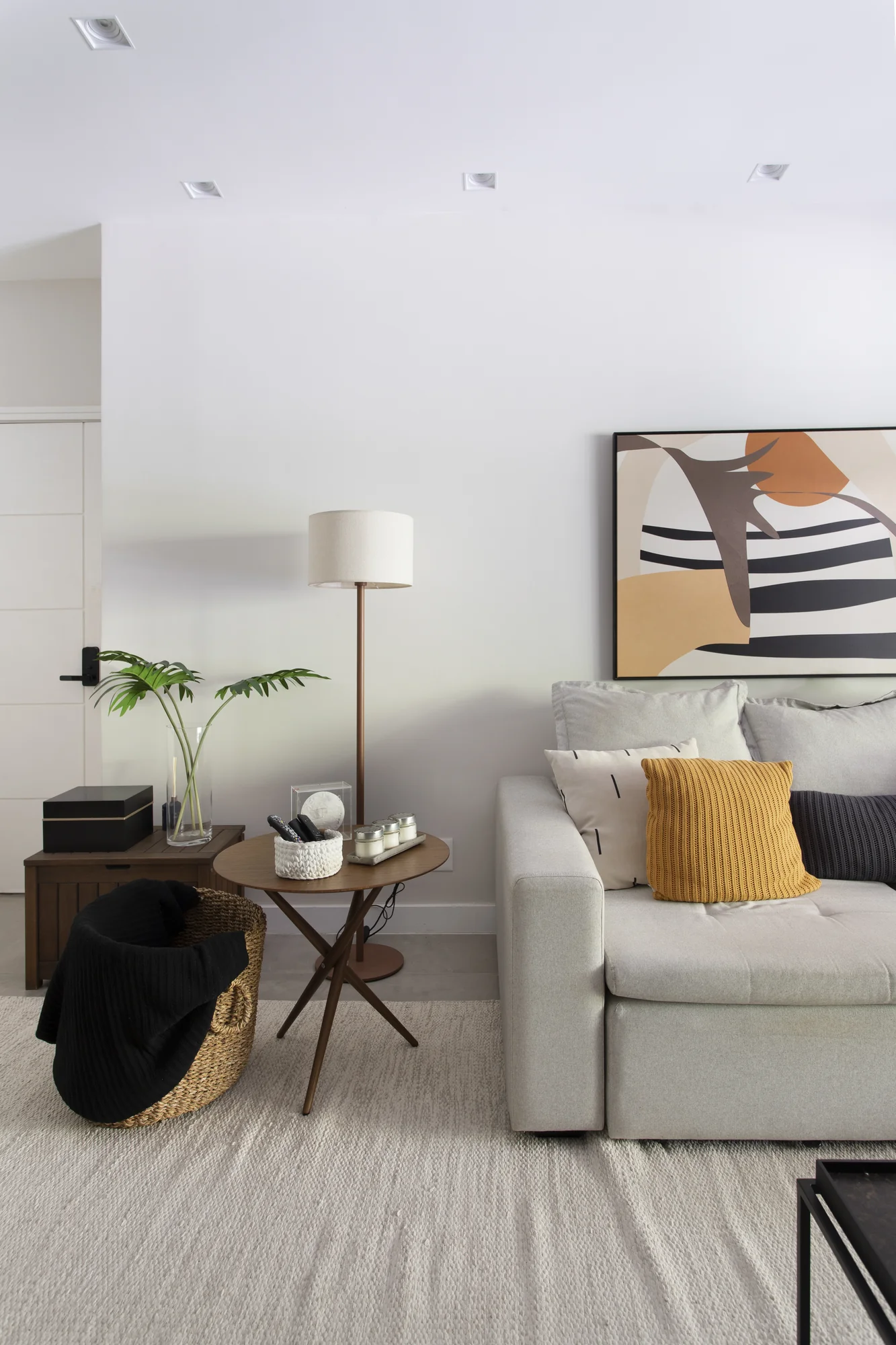 Canto do living com luminária de piso, mesa lateral e quadro geométrico