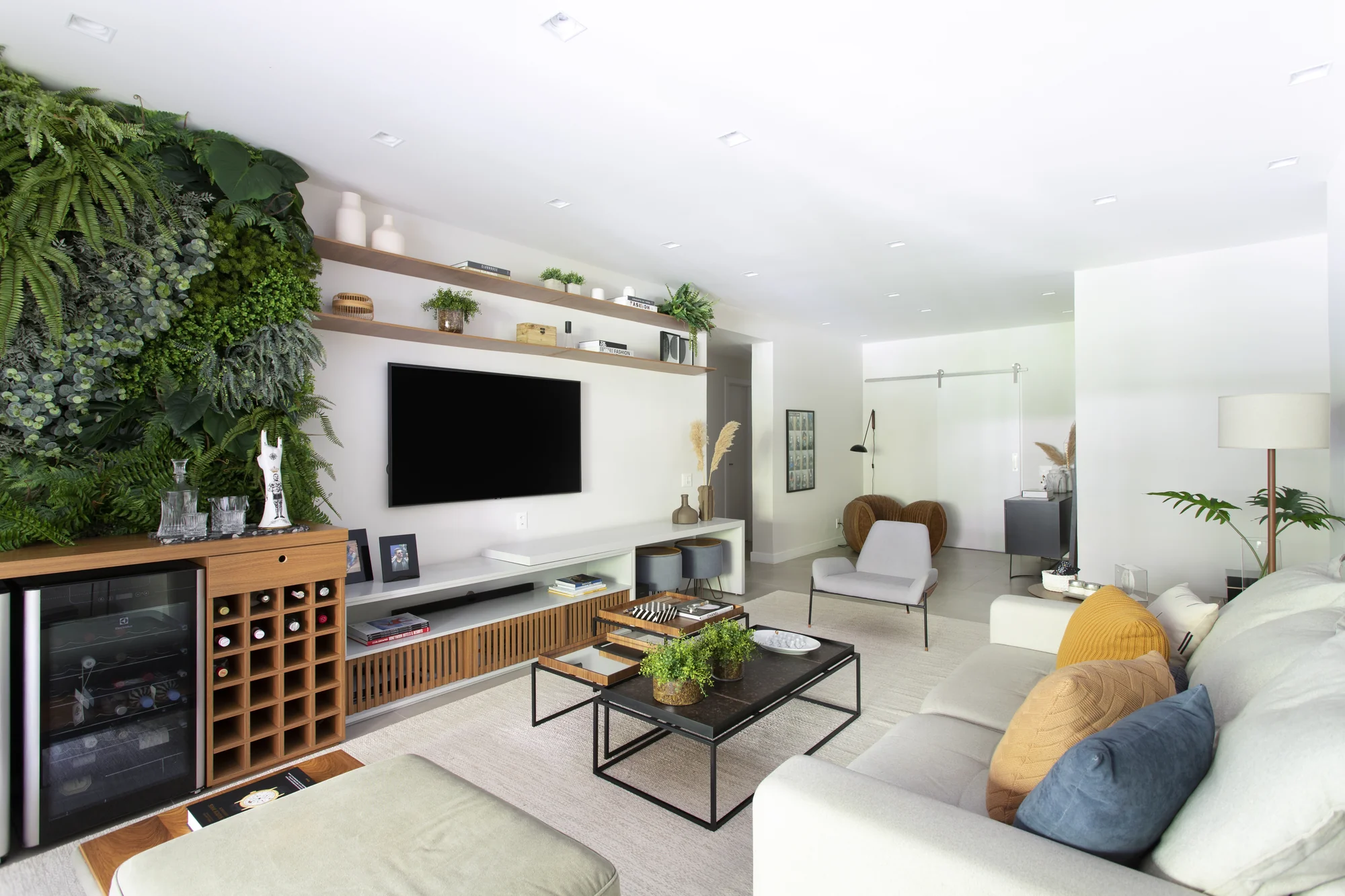 Living com jardim vertical, painel de madeira e bar com adega
